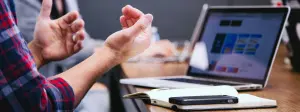 persona hablando con otro colega con movimiento de manos, frente a un computador